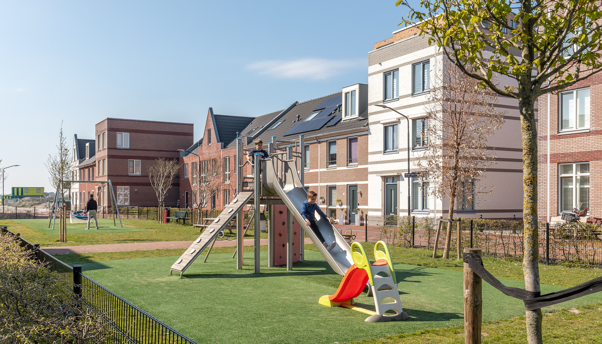 kinderen spelen in speeltuintje achter woningen. 